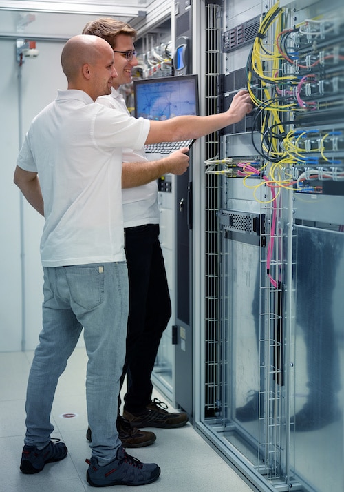 two IT professionals with notebook in server data center room solving a problem